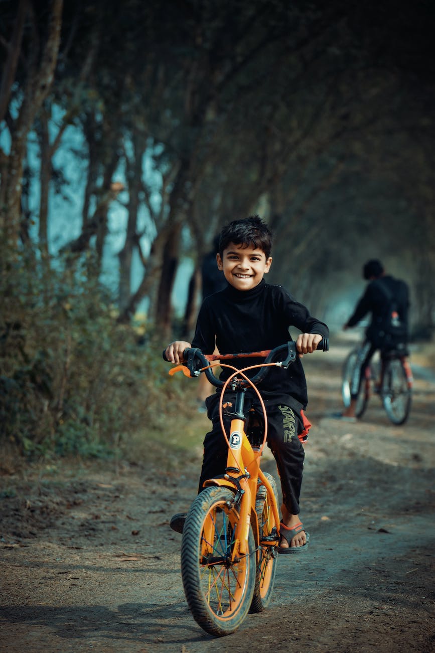 imagem de criança sorridente andando sobre bicicleta laranja em um caminho de terra.